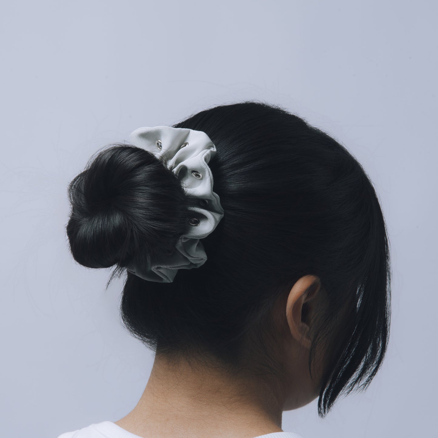 Person with a bun holding a scrunchie against a light gray background