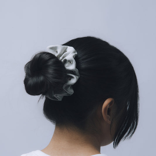 Person with a bun holding a scrunchie against a light gray background